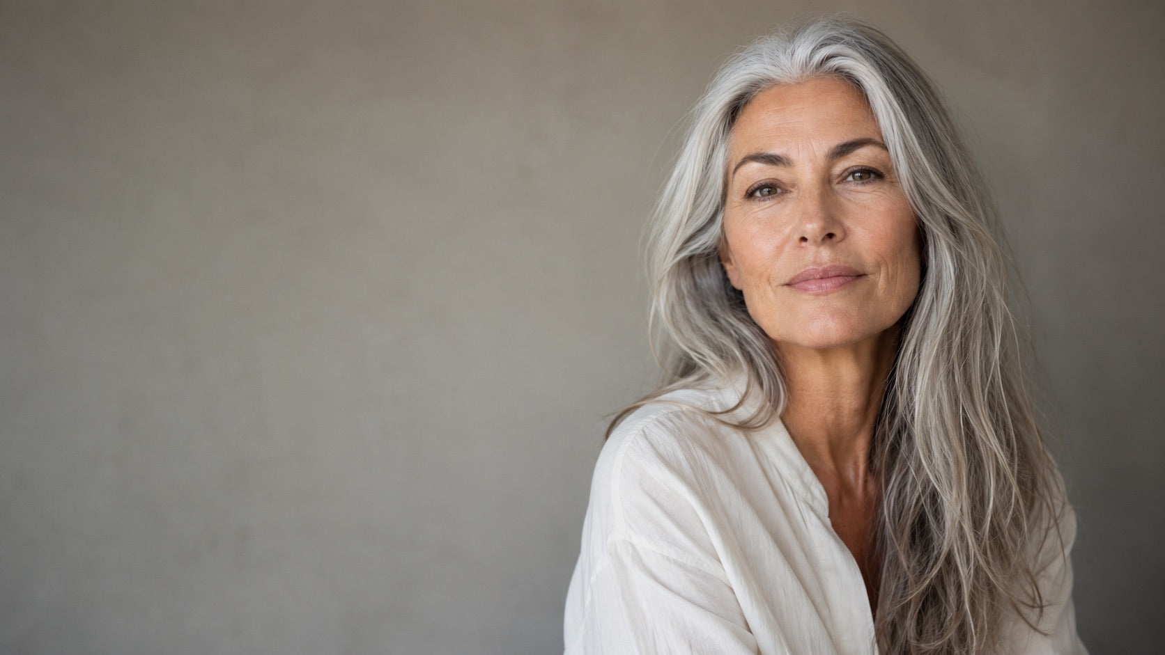 Portrait of a woman with silver-grey hair against a warm grey wall